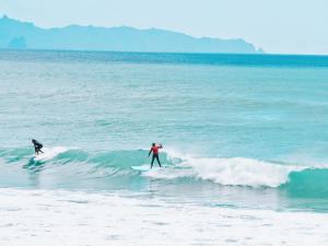 Te AraiAotearoa Surf Eco Pods的两人在海面冲浪板上挥手