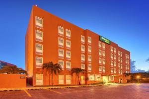 卡门城City Express Junior by Marriott Ciudad del Carmen的一座大型的橙色建筑,停车场内种植了棕榈树