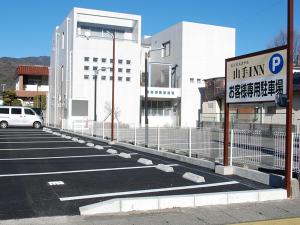 Iidamachiビジネスホテル 山手INN的大楼前有标志的停车场