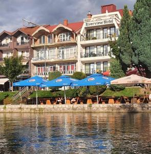 斯特鲁加Struga Riverview Hotel的水边的蓝色遮阳伞和椅子的酒店