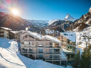 采尔马特Matterhorn FOCUS Design Hotel的一座雪中建筑,背景是群山