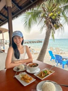 沙美岛Samed Seaside Resort - เสม็ด ซีไซด์ รีสอร์ท的坐在餐桌旁的女人,在海滩上吃点东西