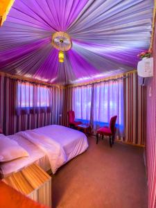 瓦迪拉姆Alora Wadi Rum Luxury的一间卧室设有紫色天花板、一张床和椅子