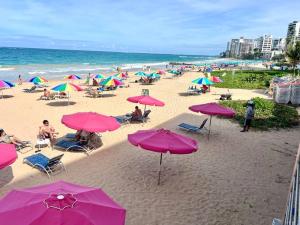 圣胡安Condado Lux Oceanfront Tantra Ap的一群人坐在海滩上,拿着粉红色的遮阳伞