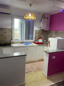 Ez Zahracosy Furnished appartment的厨房配有白色橱柜、紫色墙壁和窗户。