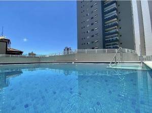 大普拉亚Apto ótima localização a 100m da Praia, Piscina, Ar Condicionado, Garagem e Portaria 24h的一个大型蓝色游泳池,其建筑背景为: