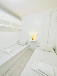马尼拉Backpackers Homestay - NomadsMNL的白色客房的两张床,配有灯