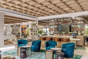 德尔雷比奇The Ray Hotel Delray Beach, Curio Collection By Hilton的大堂设有带蓝色椅子和电视的酒吧