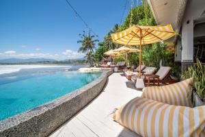 普卢坎Bombora Medewi的毗邻大海的带椅子和遮阳伞的游泳池