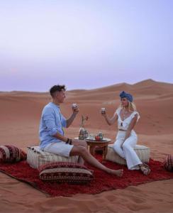 梅尔祖卡Desert Berber Camp的坐在沙漠中的男人和女人喝着饮料
