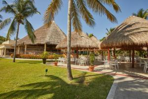 艾库玛尔Bahia Principe Grand Coba - All Inclusive的餐厅设有桌子和稻草伞,种有棕榈树
