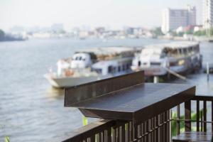 曼谷NORN Riverside Bangkok Hotel - นอนริมน้ำ的黑色长凳,坐在阳台上,在水中划船