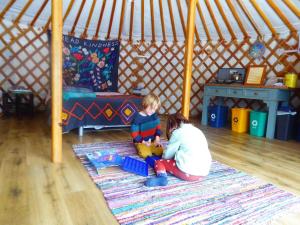 布劳顿弗内斯Wilding Yurt Stay的一名妇女和儿童在帐篷里玩耍