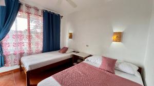 纽沃阿雷纳尔Hostal Nuevo Arenal downtown, private rooms with bathroom的客房设有两张床和一扇带蓝色窗帘的窗户。