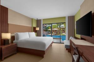 芭东海滩Courtyard by Marriott Phuket, Patong Beach Resort的一间卧室配有一张床、一台电视和一个游泳池