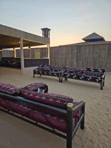 HunaywahDesert Safari Overnight Experience "Modern room with AC & Entertainment"的一群长椅坐在沙子里,靠近一座建筑物