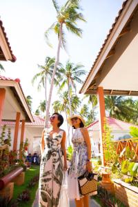 美奈Lotus Garden Muine Resort & Spa的两个女人站在棕榈树房子前面