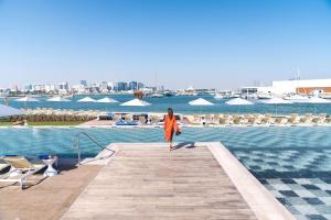 多哈Rixos Gulf Hotel Doha的穿着橙色衣服的女人在水边的码头上行走