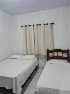 伊列乌斯Casapraiacururupe的白色客房的两张床和窗帘