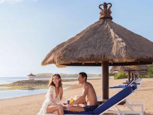 努沙杜瓦巴厘岛努沙杜瓦海滩度假村索菲特酒店的坐在海滩上,在伞下的一个男人和女人