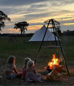 BransgoreHawthorne Field - Shoreline Escapes的三个女孩坐在帐篷前的火堆旁