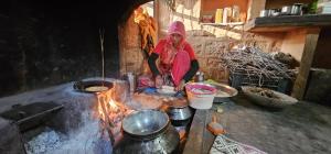 OsiānOsian Dhana Ram Ki Dhani Home Stay Osian的站在炉子旁的女人,炉子上放着锅子和锅子