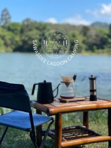 Ban Lam PiSawasdee Lagoon Camping Resort的桌子、茶壶和湖畔的椅子