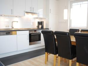 奥斯特巴特宁哈根Exkl App Kliff am Meer, W-LAN, Balkon的厨房配有白色橱柜和一张带黑色椅子的木桌
