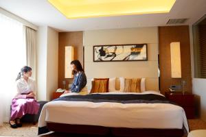 长野Kokusai 21 International Hotel的两名妇女坐在酒店房间的一个床上