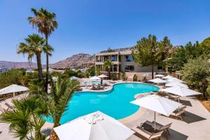 佩基罗德White Olive Premium Lindos的一个带遮阳伞和棕榈树的游泳池的度假酒店