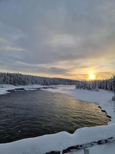JockÖverkalix Kalixalven Lodge Jockfall的雪中的小河,在背后日落