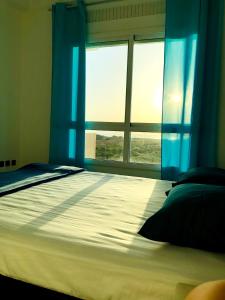 丹吉尔Fantastique Appartement avec piscine sur la plage M2的一间卧室配有一张带蓝色窗帘的床和一扇窗户