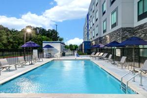 休斯顿Hampton Inn & Suites Houston East Beltway 8, Tx的一座带椅子和遮阳伞的游泳池位于一座建筑旁边