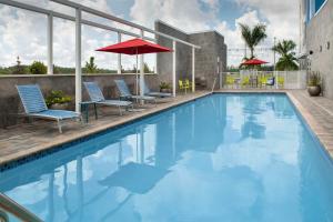 迈尔斯堡Home2 Suites by Hilton Fort Myers Airport的一座大楼内的游泳池,配有椅子和遮阳伞