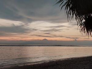 吉利特拉旺安Sahara Sands Guest House - Gili Trawangan的海滩上的日落,背景是山