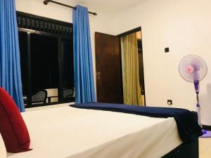 康提九霄云外旅舍的一间卧室配有一张带蓝色窗帘的床和风扇