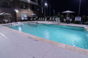 斯帕坦堡Hilton Garden Inn Spartanburg的夜间游泳池,配有椅子和遮阳伞