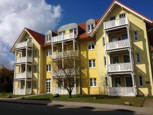 奥斯赛拜-屈隆斯博恩Strandschloesschen-Haus-II-WE-17-9871的黄色的公寓楼,设有白色阳台和一棵树