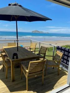 WaimaramaUltimate Beach Front的海滩上一张木桌和椅子及遮阳伞