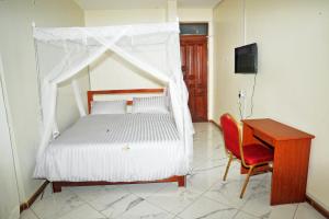 KigaramaApollo Inn Fortportal的一间卧室配有一张带天蓬的床和一张书桌