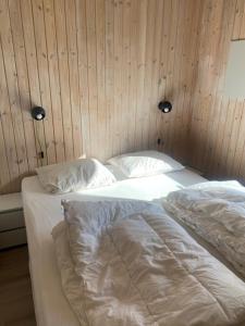 BønnerupSkønt sommerhus tæt på skov, strand og hyggeligt havnemiljø的一间卧室配有两张带白色床单和木墙的床。