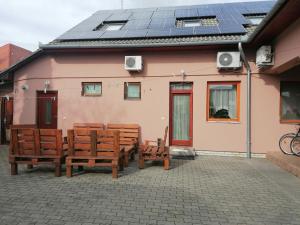 KunszentmártonIglódi Panzió的一组长椅,在一座粉红色的建筑前,设有太阳能电池板