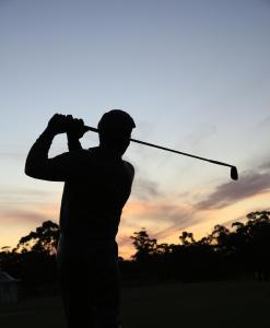 墨尔本The Victoria Golf Club的一名男子在高尔夫球俱乐部挥手,背着日落