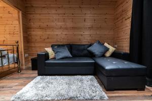 邓加文The Hen Harrier - 4 Person Luxury Glamping Cabin的一张黑色皮沙发,位于一个木墙房间内