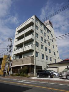 上野原市上野原阁路线酒店的一座高大的白色建筑,前面有汽车停放