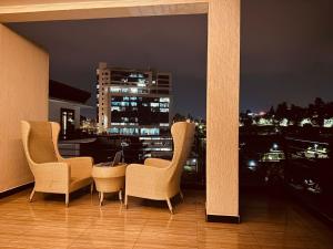 基加利AMORA APARTMENT的阳台上的三把椅子和一张桌子在晚上