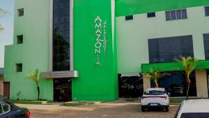 马拉巴Amazônia Palacce Hotel的一座绿色的白色建筑,前面有停车位