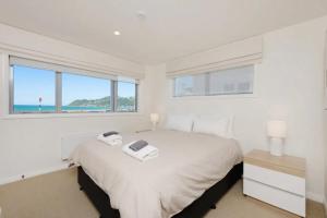 惠灵顿Lyall Bay Parade Apartment的白色卧室设有大床和窗户