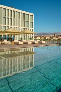 斯普利特Hotel Ambasador的游泳池旁的酒店拥有椅子和遮阳伞