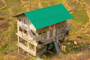 MalothaDhauladhar Woodhouse的山丘上带绿色屋顶的房子